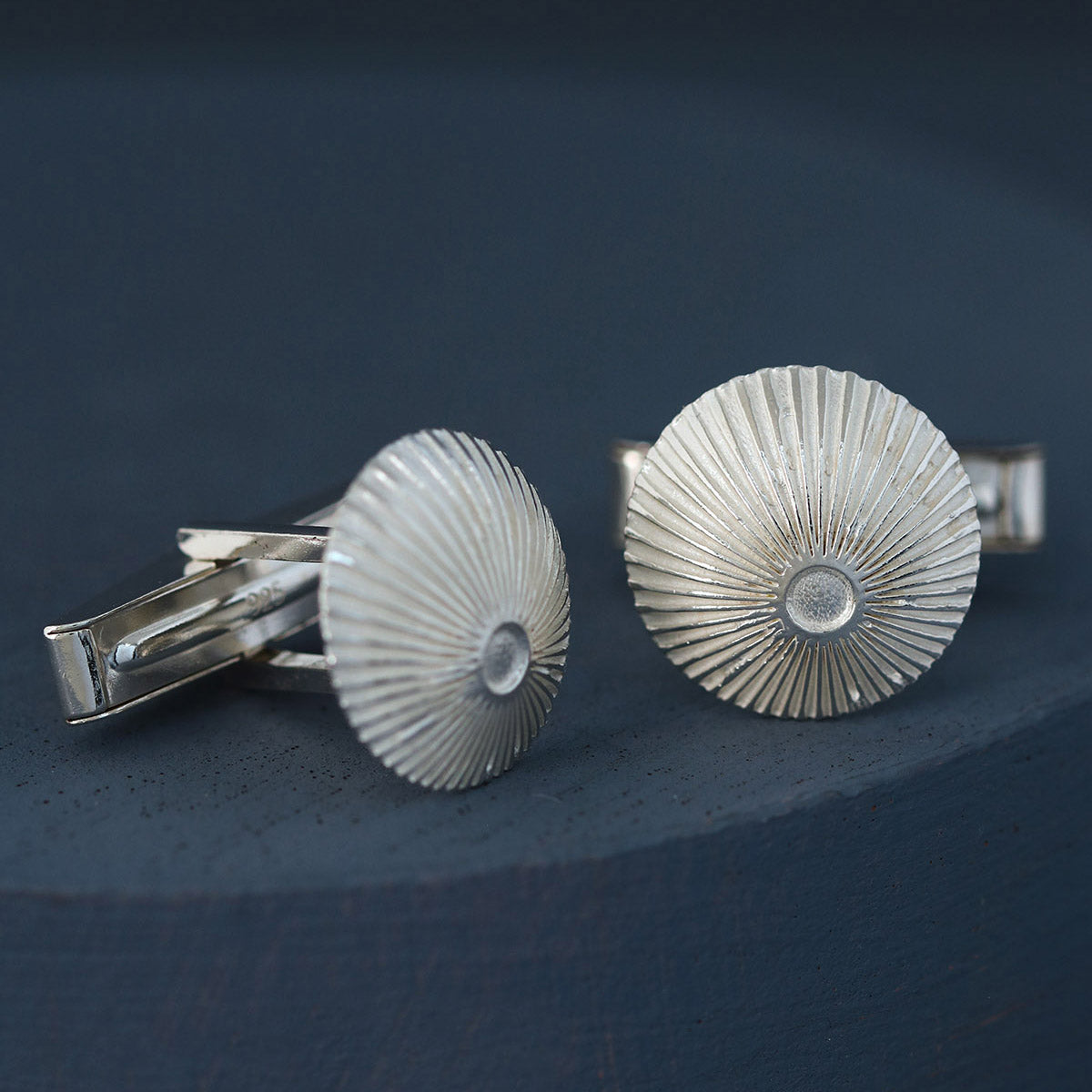 Single round cufflink close-up on deep blue background showing quality engraving – sterling silver cufflinks for Christmas gifting.