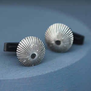 Sterling silver and black cufflinks with textured sunburst engraving, photographed on deep blue background, ideal best man or groomsmen gift.