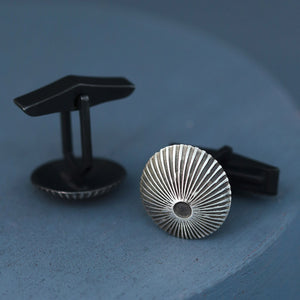 Pair of silver and black cufflinks displayed on deep blue background, modern geometric design for luxury birthday gift for him.