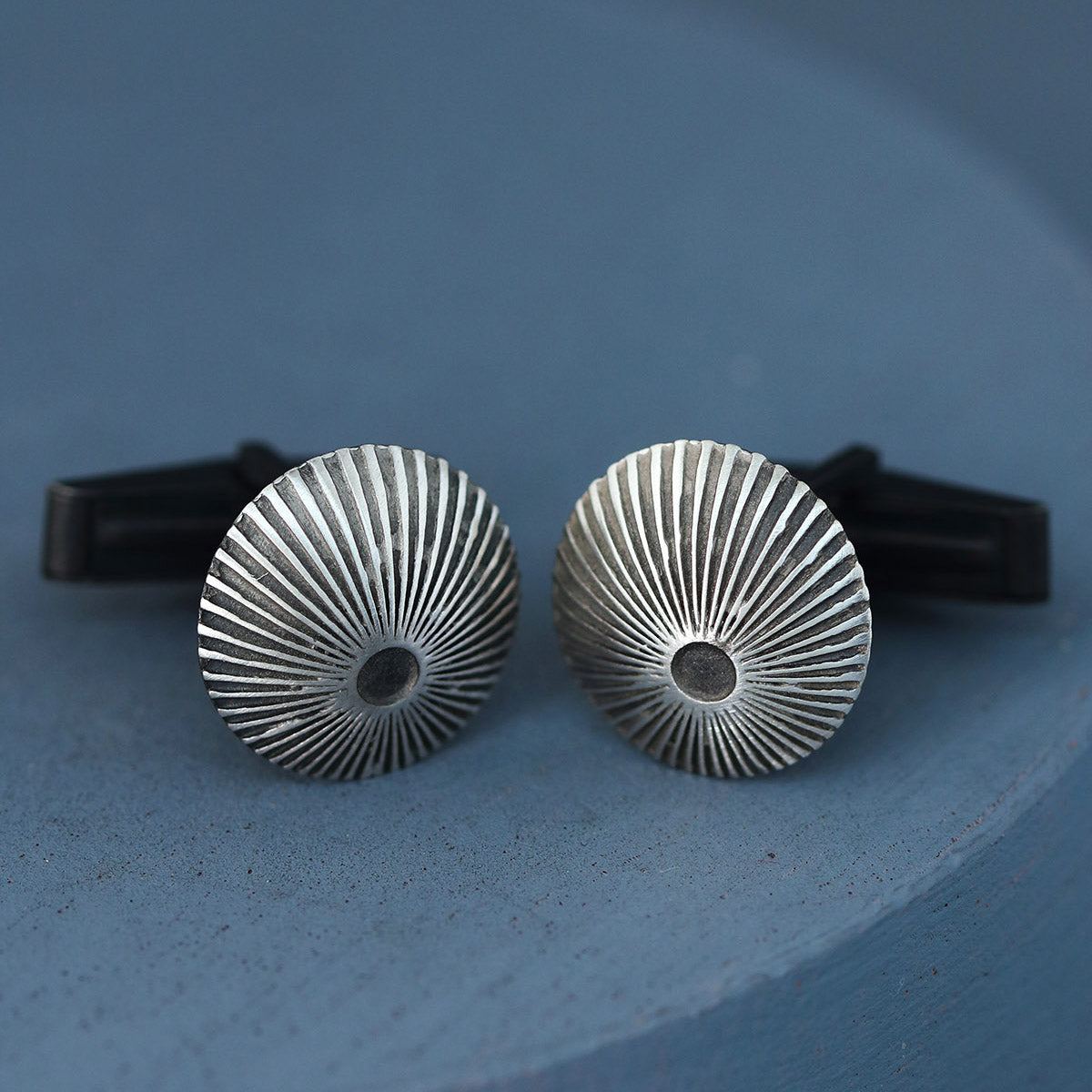 Silver and black cufflinks with engraved Art Deco design photographed on deep blue background, ideal mens luxury cufflinks for wedding day style.