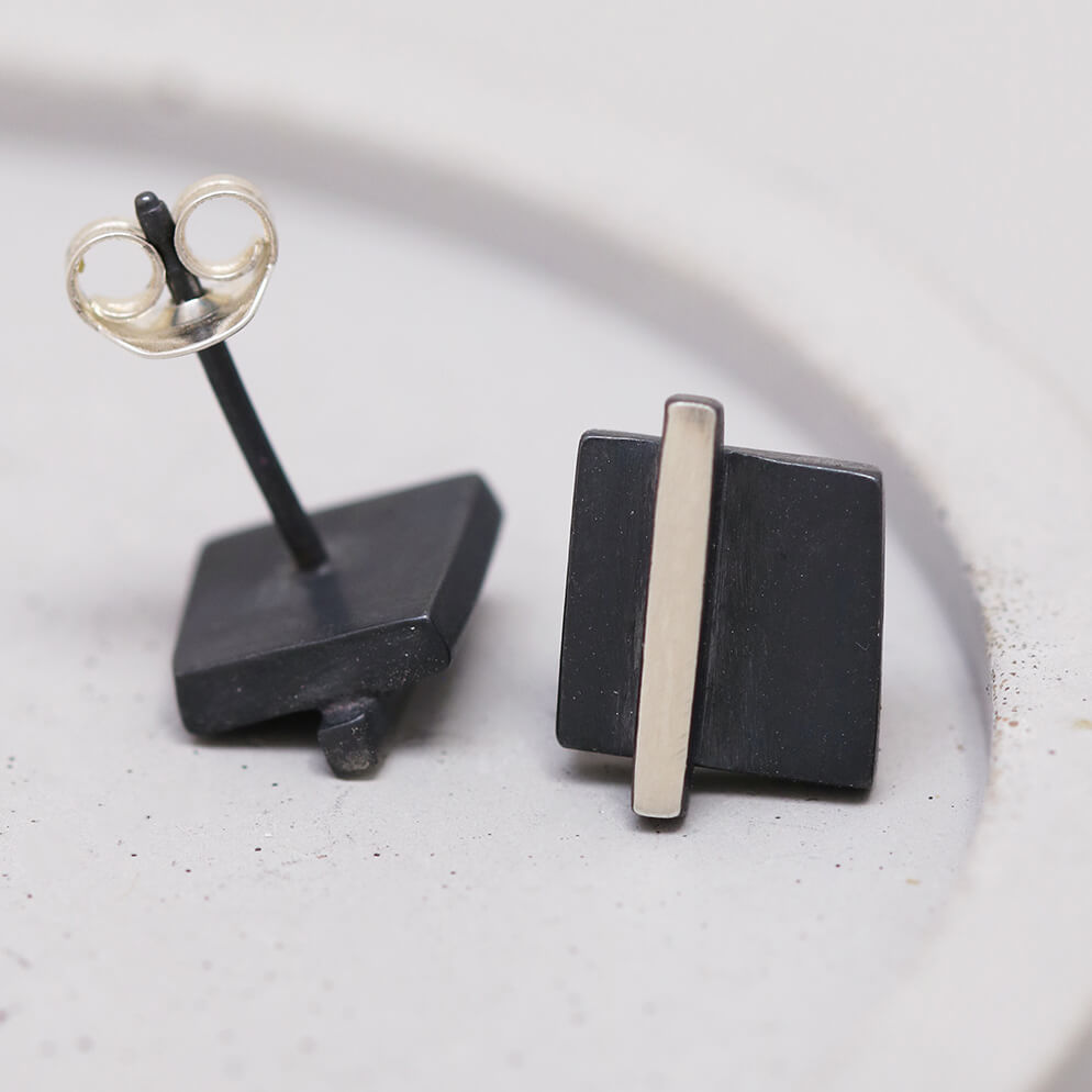 Close-up of silver and black earrings on a grey dish showing the polished silver line, great anniversary gift idea.