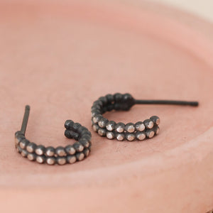 Small silver and black hoop earrings with beaded double hoop design on a pink dish
