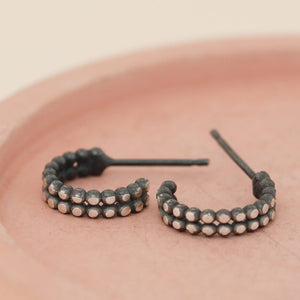 Little black hoop earrings with contrasting silver finish laid on a pink dish