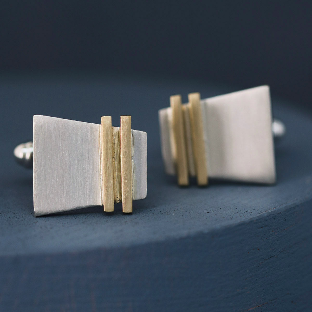 Side-angle shot of silver and gold cufflinks on deep blue fabric, showing oxidised silver contrast; stylish luxury cufflinks for birthday or milestone celebrations.
