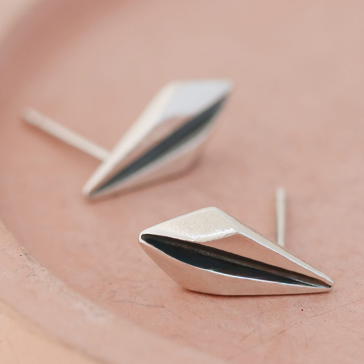 Silver art deco earrings on pink dish with soft lighting to show polished finish.