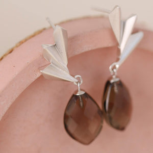 Side angle view of silver and smoky quartz earrings on a pink dish, focusing on light reflection and craftsmanship; ideal for milestone gifting.