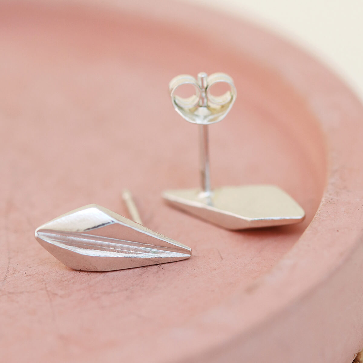 Simple, modern art deco stud earrings placed on a pink dish, perfect for elevating everyday outfits or gifting to Art Deco jewellery fans.