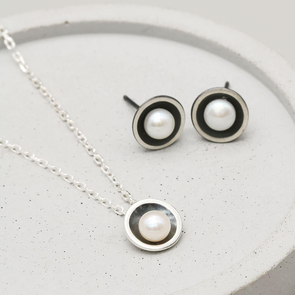Black pearl pendant necklace displayed with matching oxidised sterling silver pearl stud earrings on a dark grey dish.