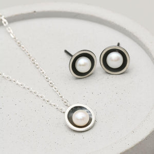 Black pearl pendant necklace displayed with matching oxidised sterling silver pearl stud earrings on a dark grey dish.
