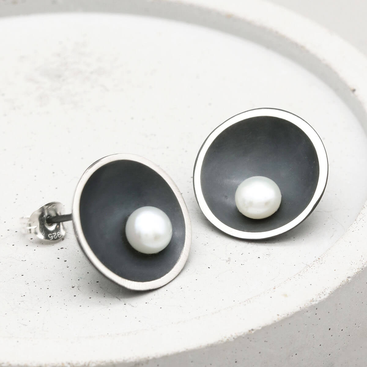 Genuine freshwater black pearl stud earrings in handcrafted oxidised sterling silver photographed on a grey ceramic dish.