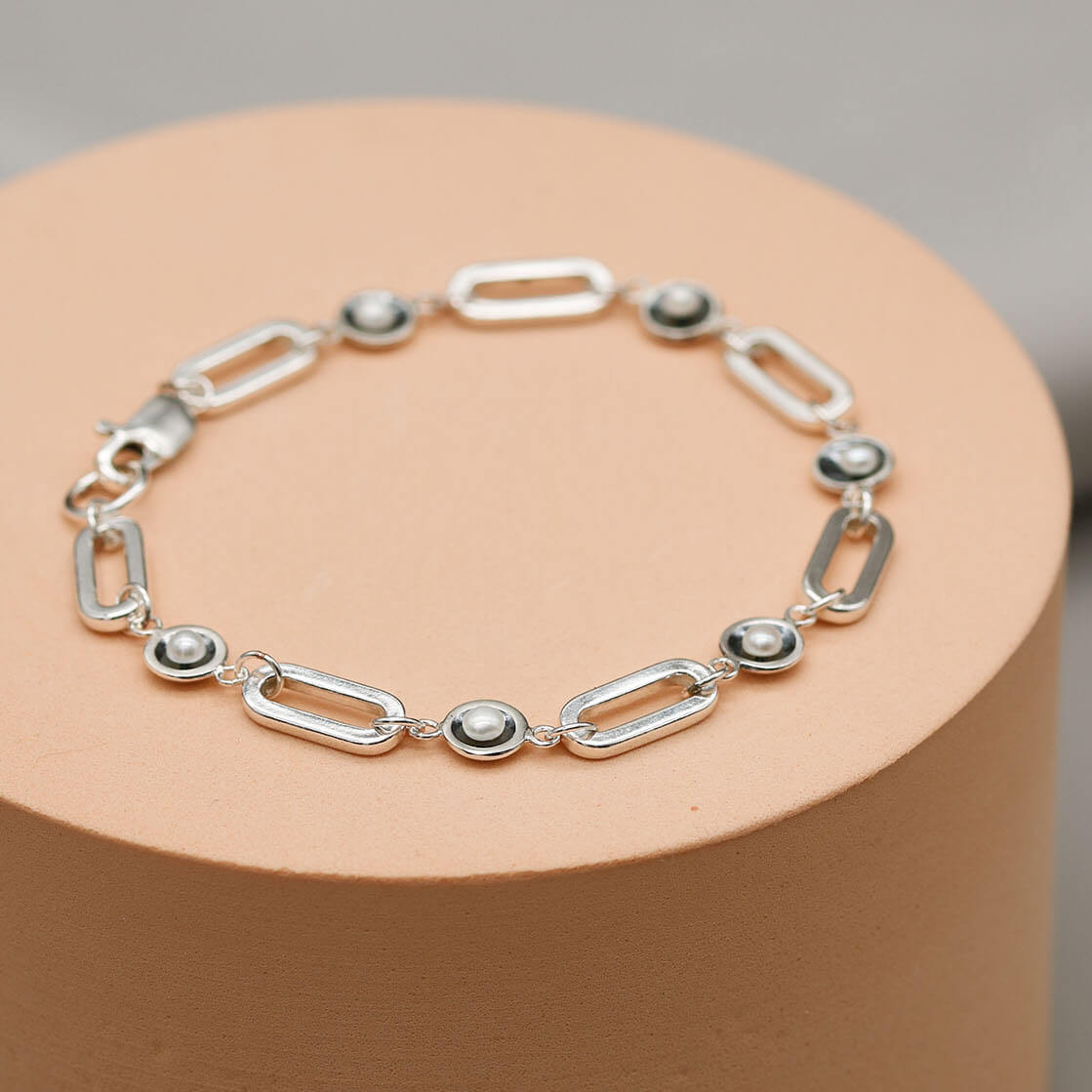 Contemporary sterling silver pearl bracelet with oxidised pearl settings displayed on a pink pedestal against a grey background.