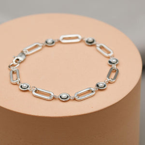 Contemporary sterling silver pearl bracelet with oxidised pearl settings displayed on a pink pedestal against a grey background.