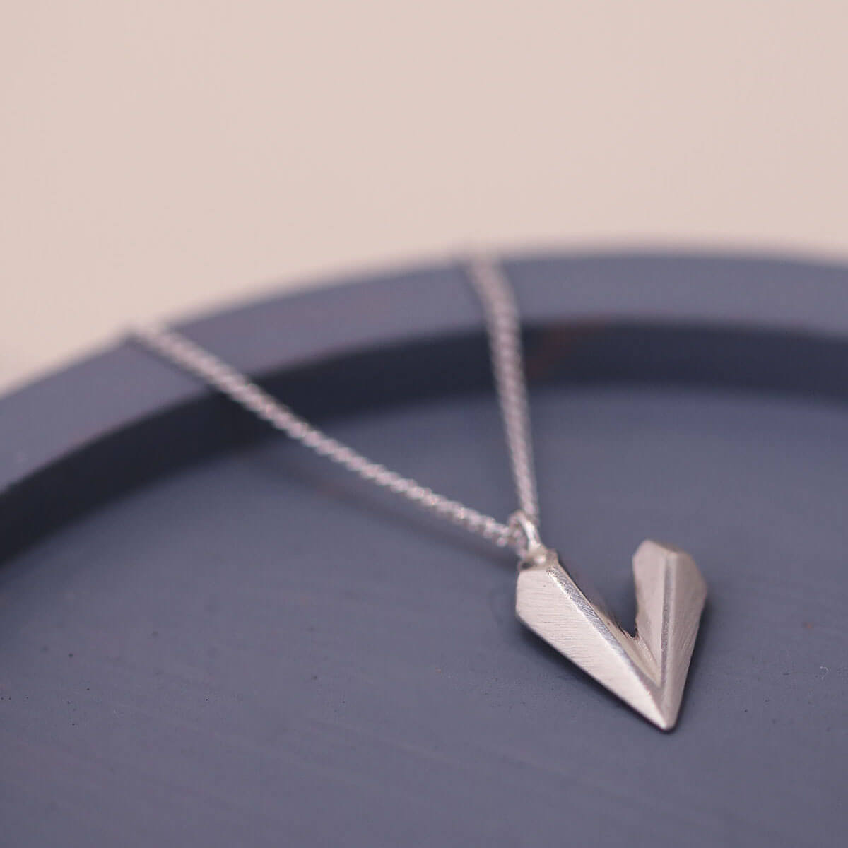 Faceted heart shaped necklace laid on a blue dish, a delicate sterling silver dainty heart necklace for gifting