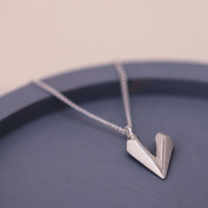 Faceted heart shaped necklace laid on a blue dish, a delicate sterling silver dainty heart necklace for gifting
