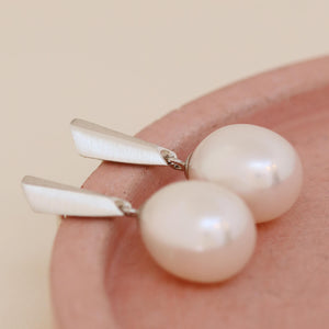 Detail shot of geometric sterling silver tops and large pearls displayed on a pink dish for a refined, feminine presentation.