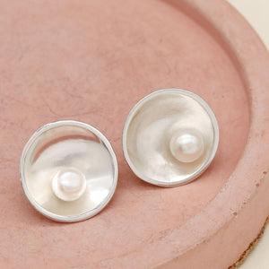 Freshwater pearl stud earrings handcrafted in sterling silver with an elegant Art Deco-inspired design on a pink dish.