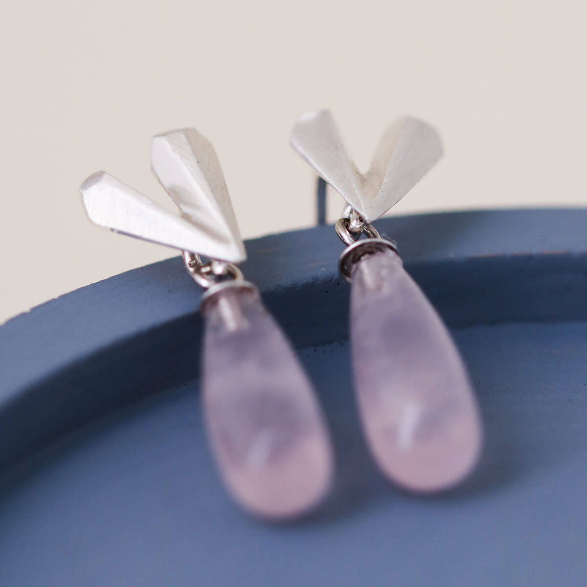 Heart dangle earrings handmade in sterling silver with blush rose quartz, Pink heart earrings styled on a blue dish for product photography