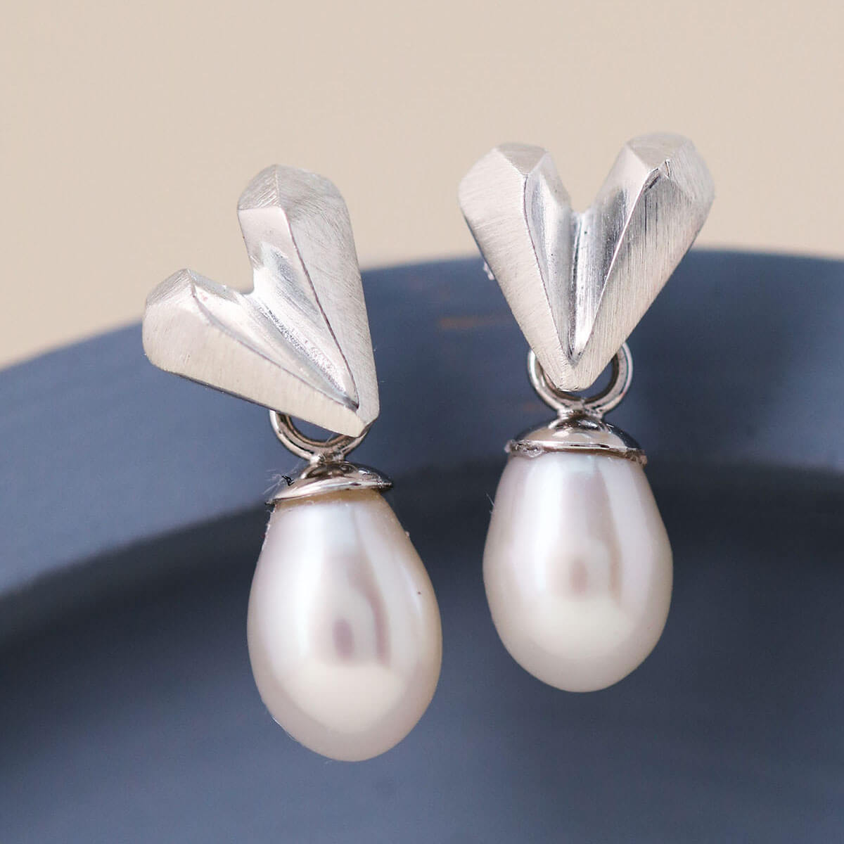 Heart pearl earrings in sterling silver displayed on a blue dish, showing faceted heart stud and white pearl drop, silver wedding earrings for bridesmaids
