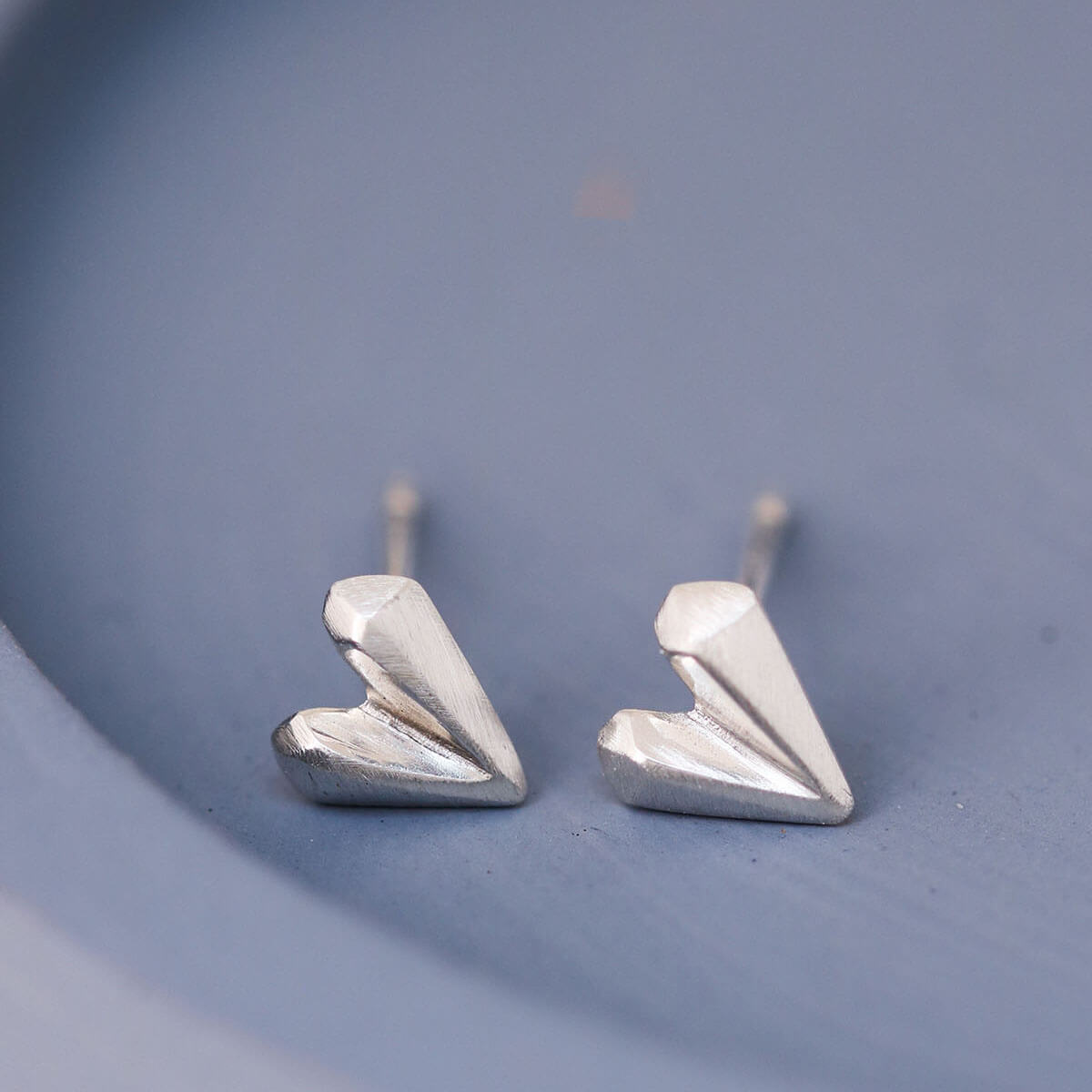 Detailed view of silver heart stud earrings on blue dish, dainty love heart earrings for birthday gifting