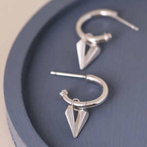 Silver hoop earrings with heart charm shown on a blue dish, sterling silver charm hoops with faceted heart drop