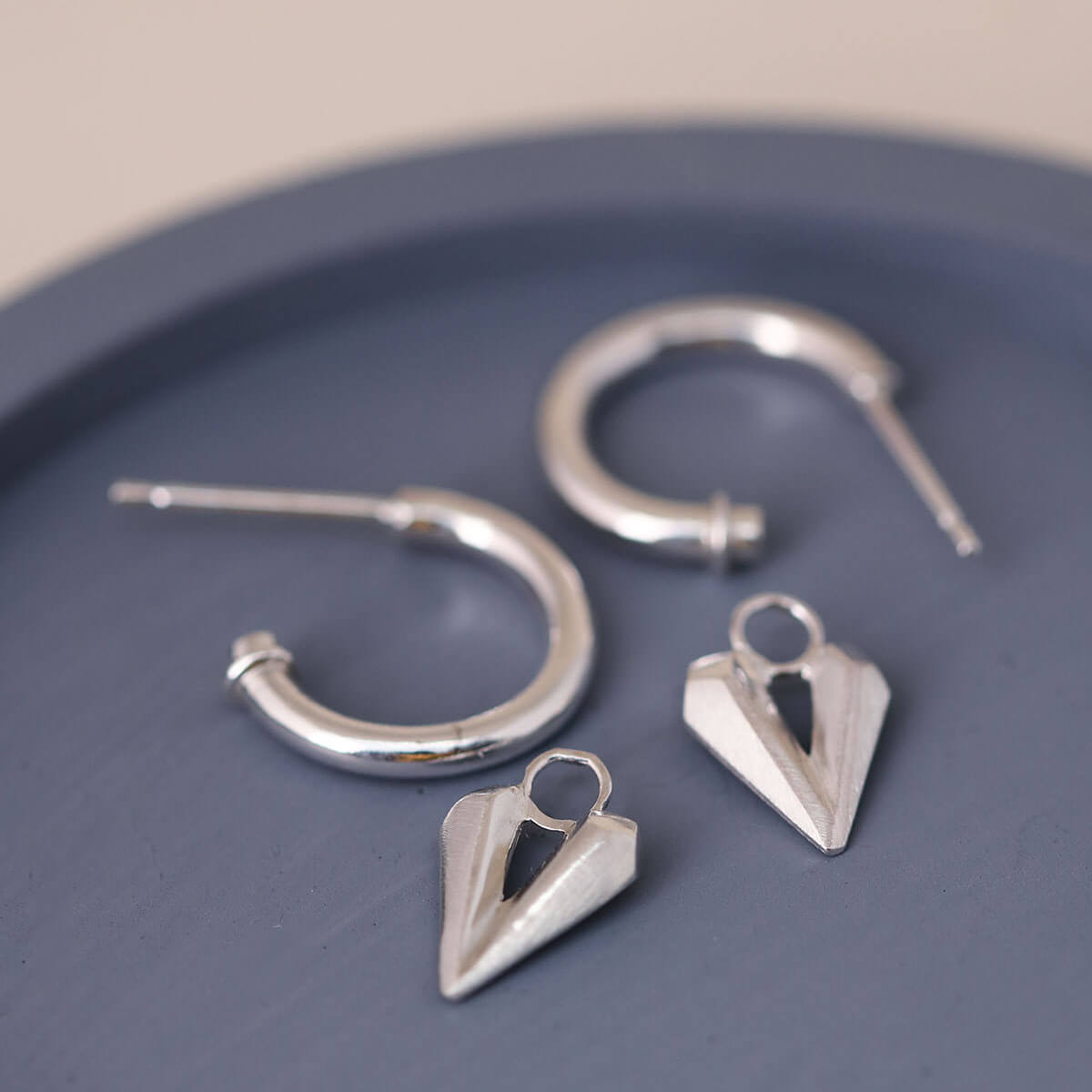 Silver hoop earrings with heart charm styled on a blue dish, modern hoops with hearts and soft movement