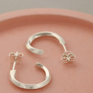 Sterling silver hoop earrings for women photographed on a pink dish, small sculpted silver hoop stud earrings gift for her