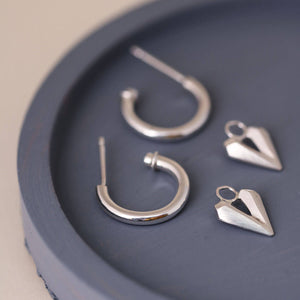 Silver hoop earrings with heart charm laid on a blue dish, delicate hoops with hearts in sterling silver