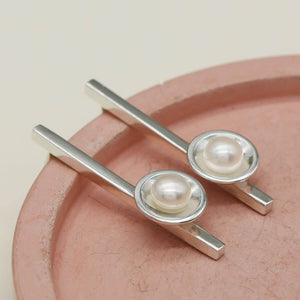 Pearl hanging earrings featuring polished sterling silver and freshwater pearls on a pink ceramic dish.