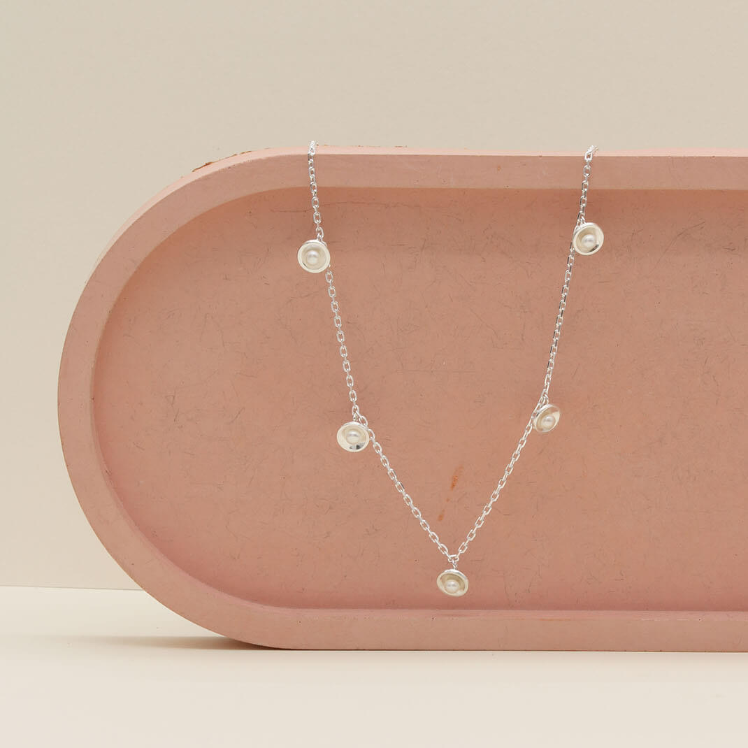 Sterling silver pearl chain necklace displayed on a pink ceramic dish, showing the adjustable 16 to 18 inch chain and delicate freshwater pearl stations.