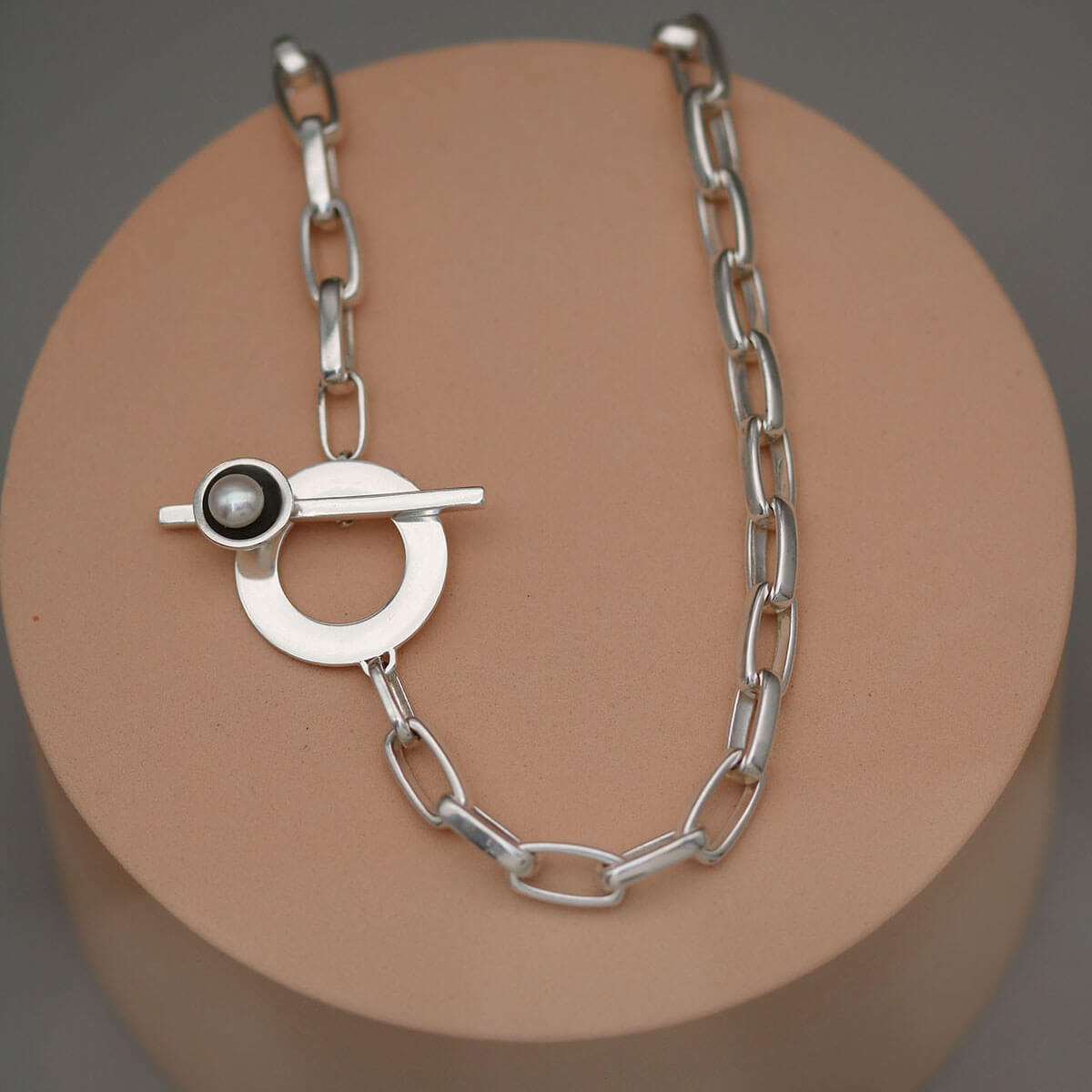 Contemporary chunky pearl necklace with sterling silver toggle clasp and large freshwater pearl displayed on a pink display stand.