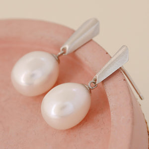 Silver dangle pearl earrings placed on a pink dish, highlighting the blend of modern silver design and classic pearl elegance.