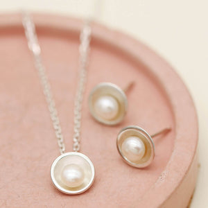 Handmade silver pearl pendant necklace shown alongside matching sterling silver pearl stud earrings on a pink dish.