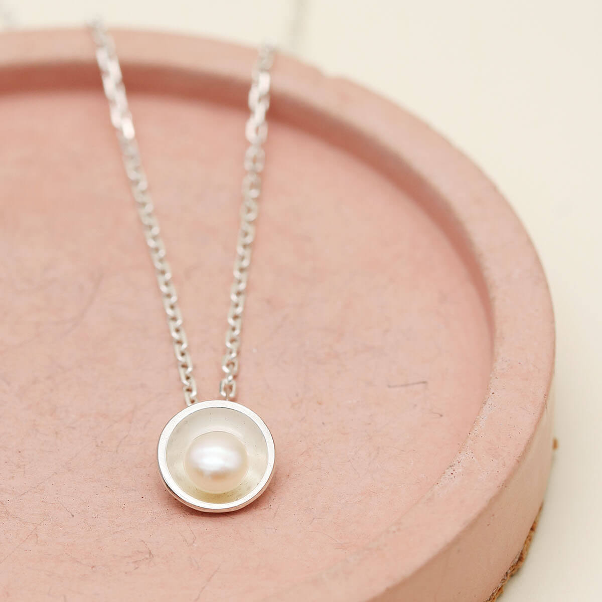 Handmade sterling silver pearl pendant necklace with a single freshwater pearl displayed on a soft pink dish.