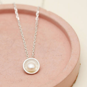 Handmade sterling silver pearl pendant necklace with a single freshwater pearl displayed on a soft pink dish.