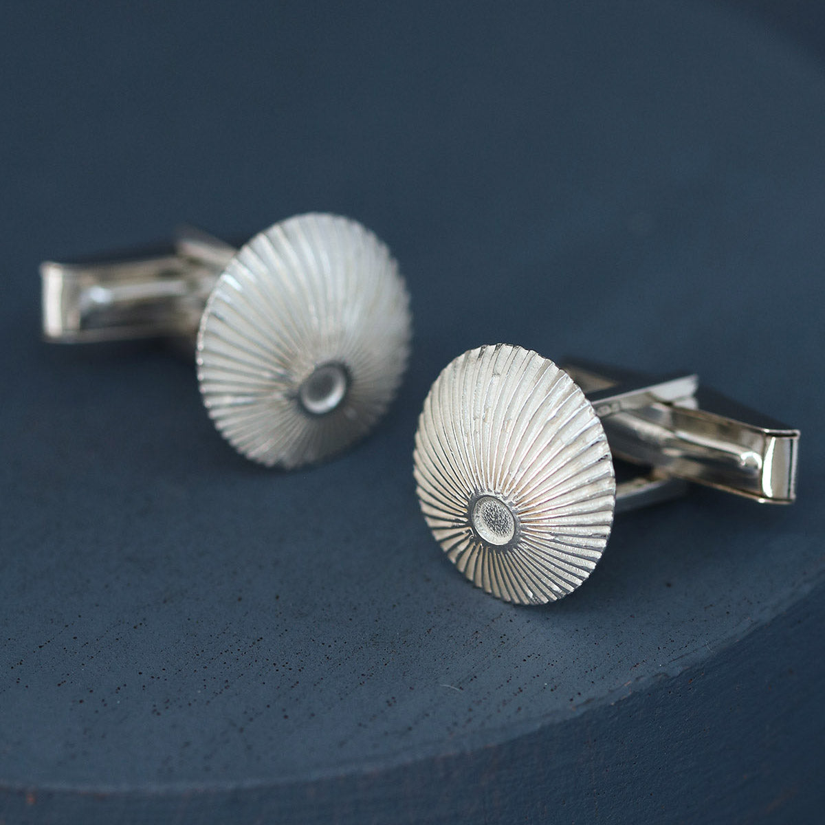 Sterling silver round cufflinks photographed on deep blue dish with soft lighting – thoughtful Valentine’s Day gift for him.