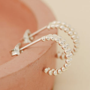 Sterling silver huggie hoops with beaded double hoop detail shown on a pink dish