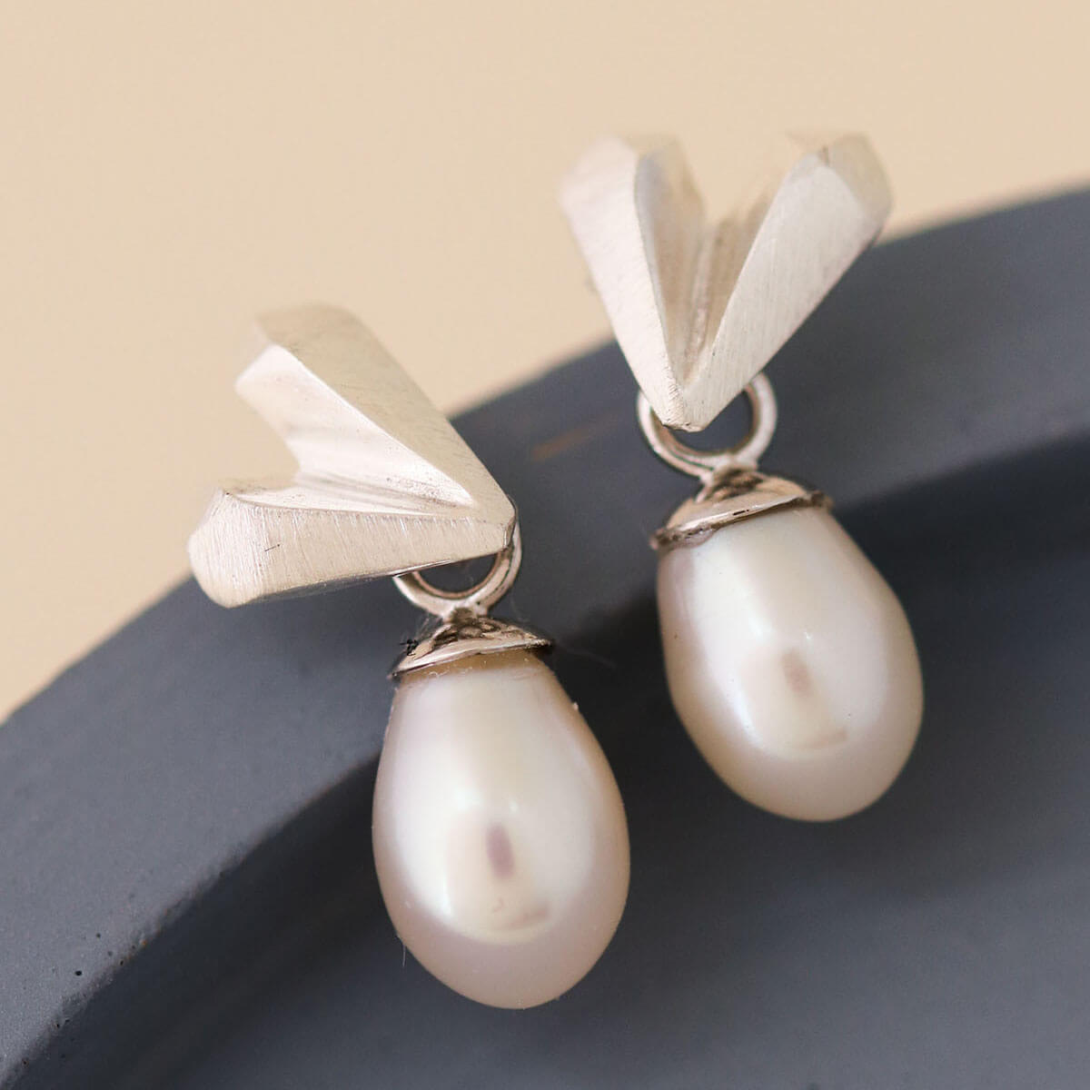 Close up of heart pearl earrings on a blue dish highlighting faceted silver heart and soft white pearl, elegant silver wedding earrings gift