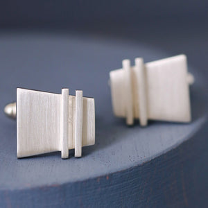 Sterling silver Modern cufflinks photographed side-by-side on a deep blue background, showcasing elegant shape and precise craftsmanship.