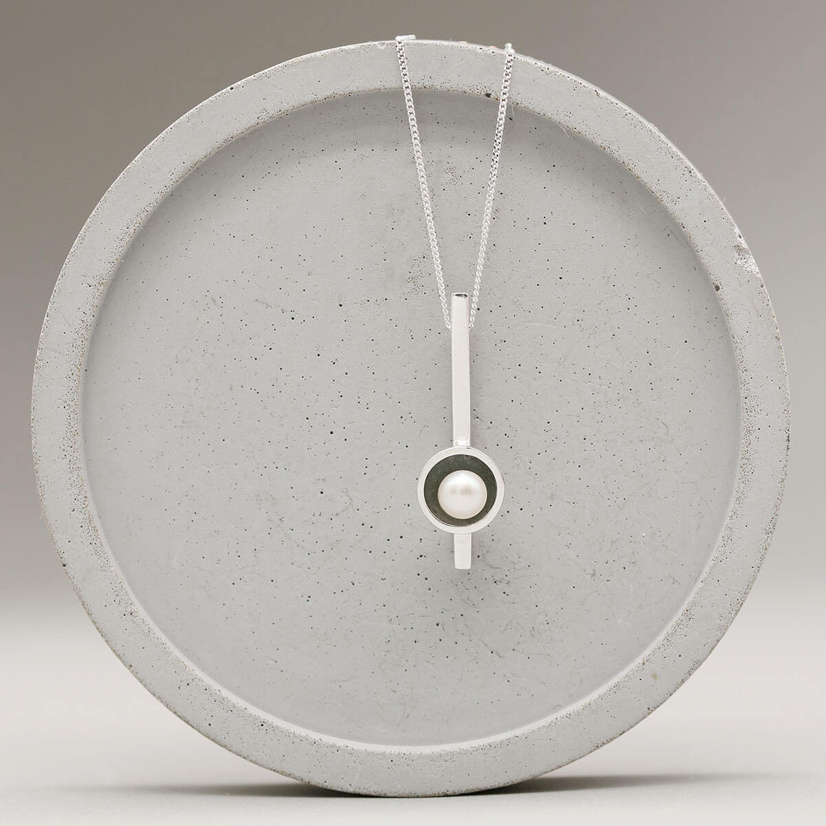 Handmade simple pearl necklace in oxidised sterling silver displayed on a grey ceramic dish.