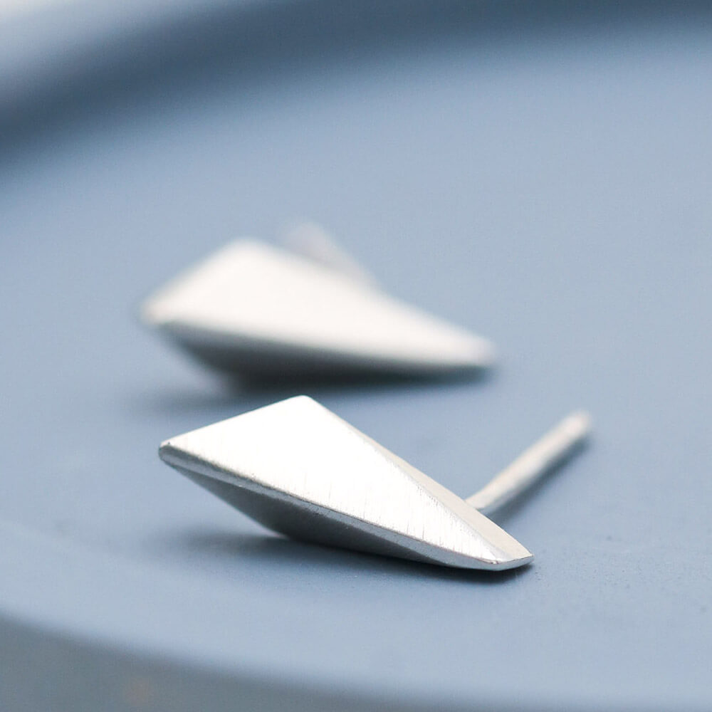 Sterling silver stud earrings with polished kite-shaped fronts on a deep blue dish, handmade small silver studs