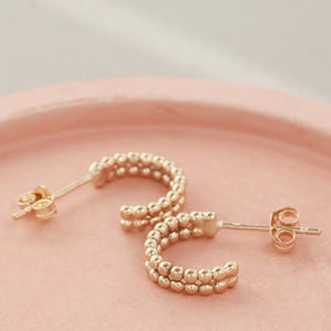 Flat-lay of small 9ct gold hoop earrings on a pink dish, showcasing the minimalist double-hoop style of these 9 carat gold hoops.