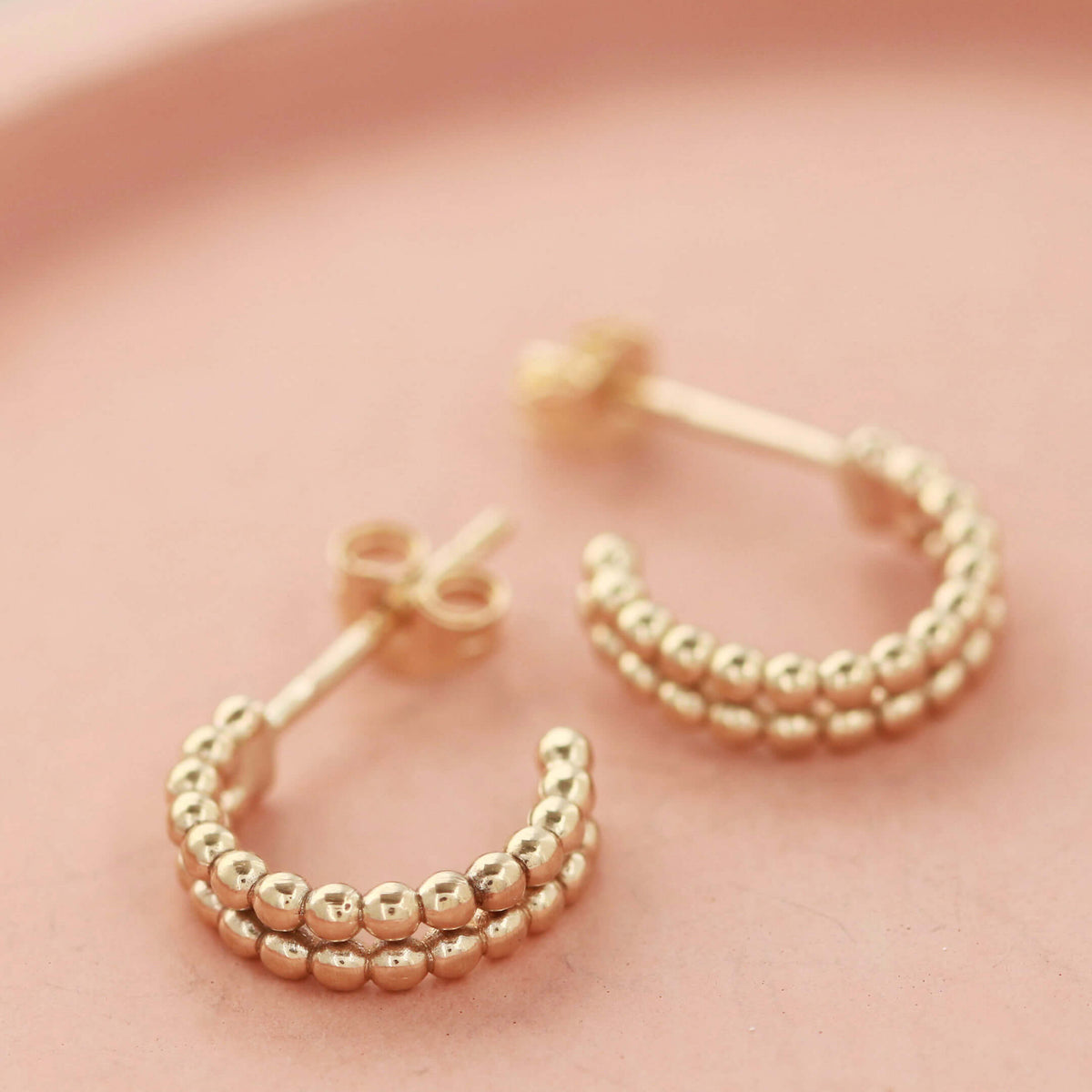 Small 9ct gold hoop earrings displayed on a pale pink dish, showing the delicate double-hoop beaded design, perfect gift for her.