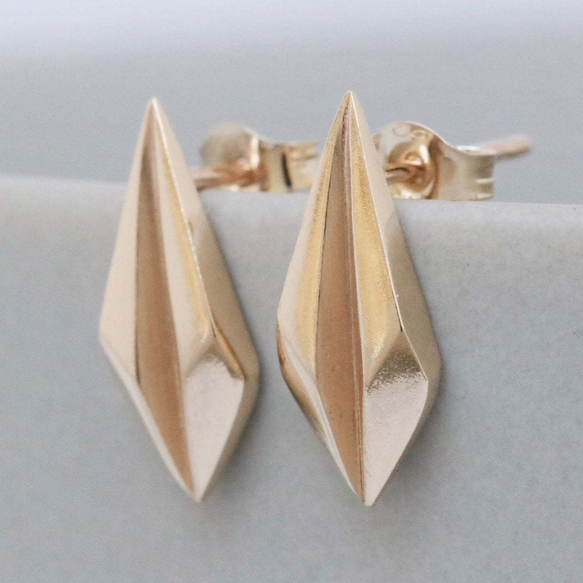 Gold art deco earrings shown flat on pale grey, solid gold geometric studs for everyday wear.