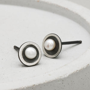 Handmade Petite Tiny Pearl Stud Earrings in oxidised sterling silver with genuine freshwater pearls displayed on a dark grey ceramic dish.
