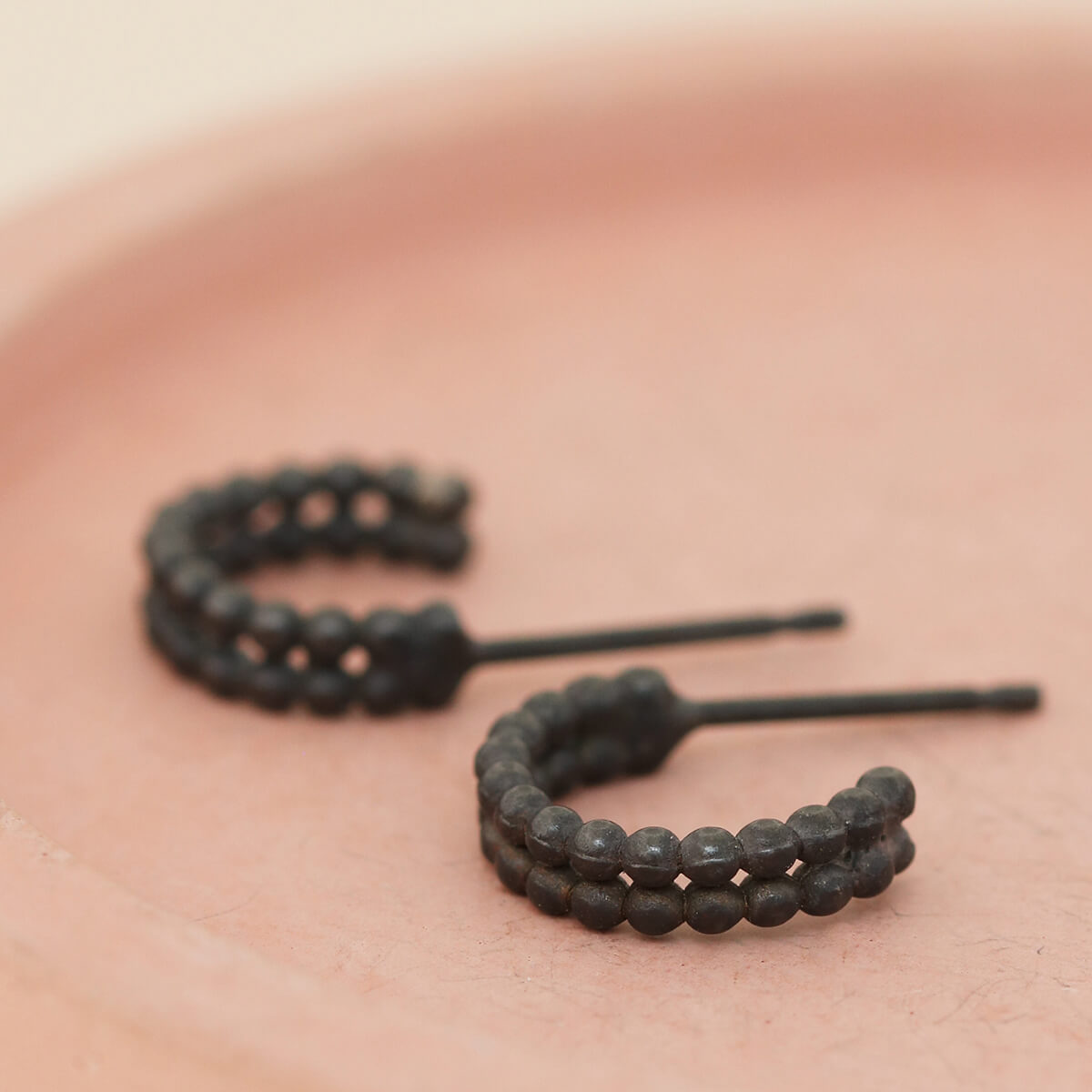 Sterling silver small black hoop earrings shown on a pink dish, everyday black hoop earrings for women