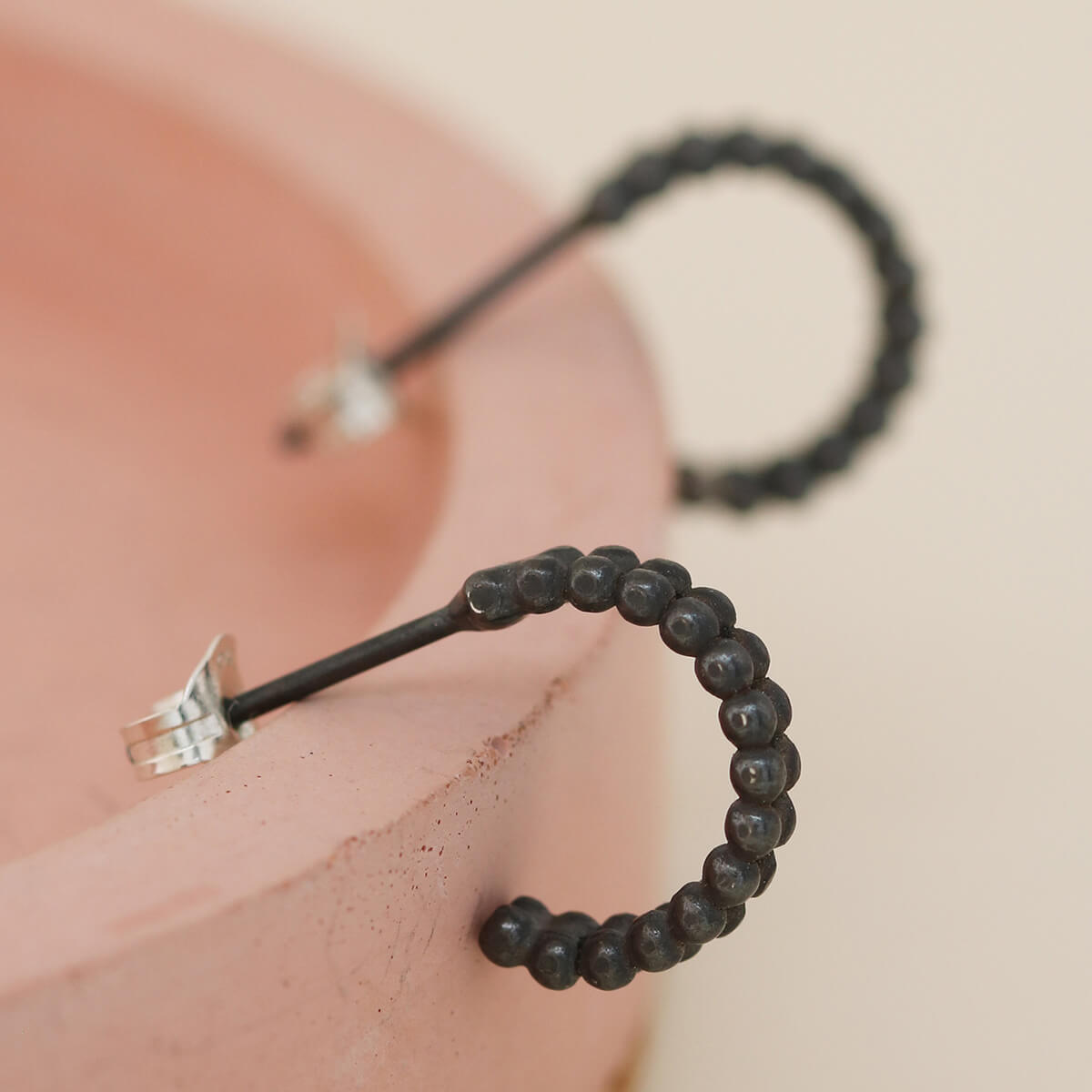 Small black hoop earrings with beaded double hoop design styled on a pink dish