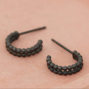 Black hoop earrings for women laid flat on a pink dish, small black hoop earrings for daily wear