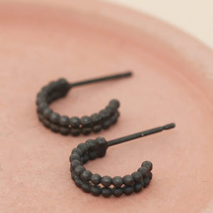 Small black hoop earrings displayed on a pink dish, minimalist sterling silver huggie design