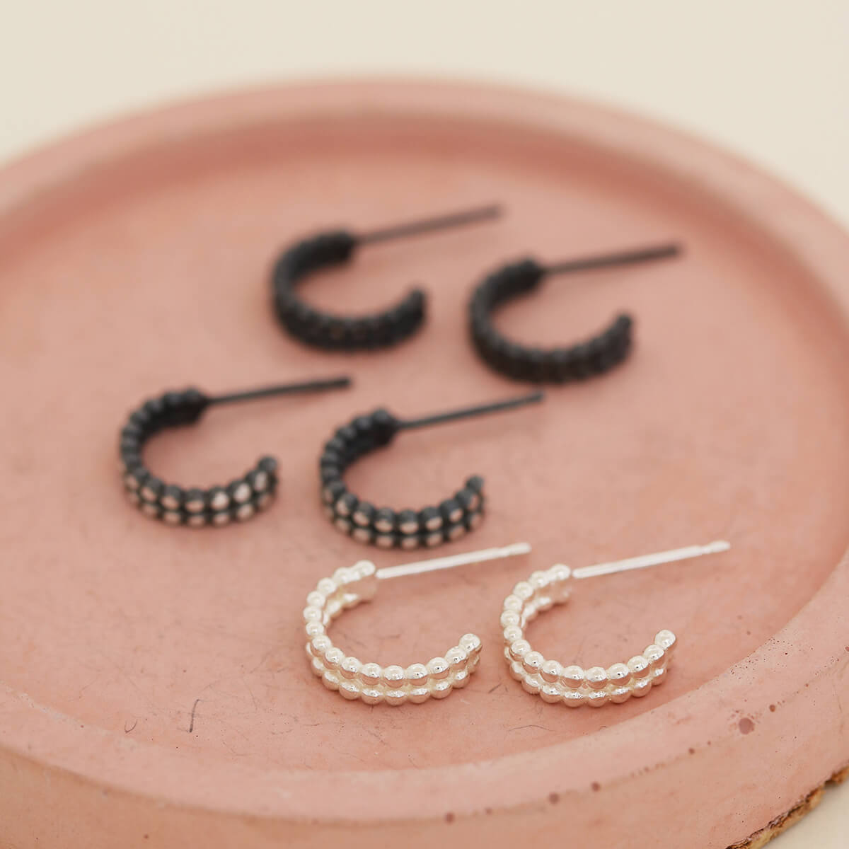 Small huggie hoop earrings showing sterling silver, black and silver finishes arranged on a pink dish