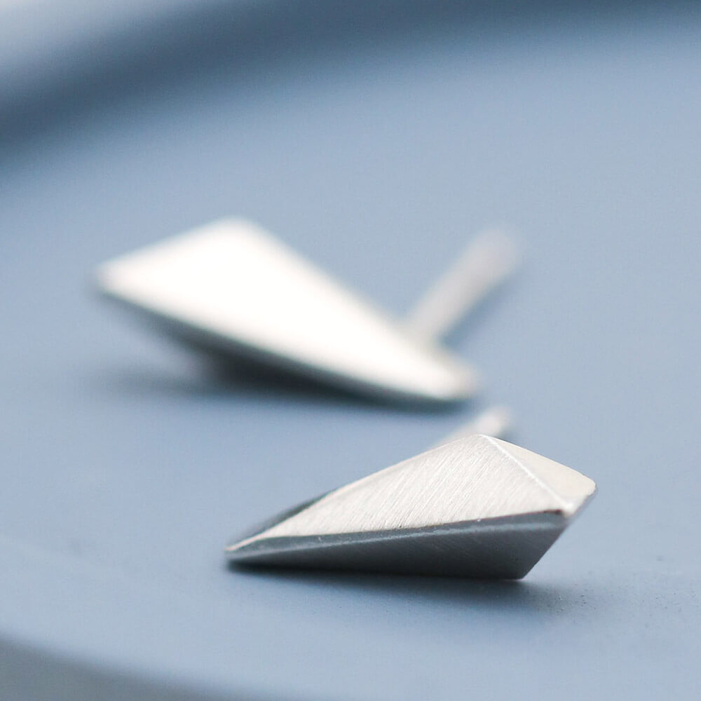 Sterling silver studs with clean Art Deco-inspired geometric lines, small silver stud earrings on a deep blue dish